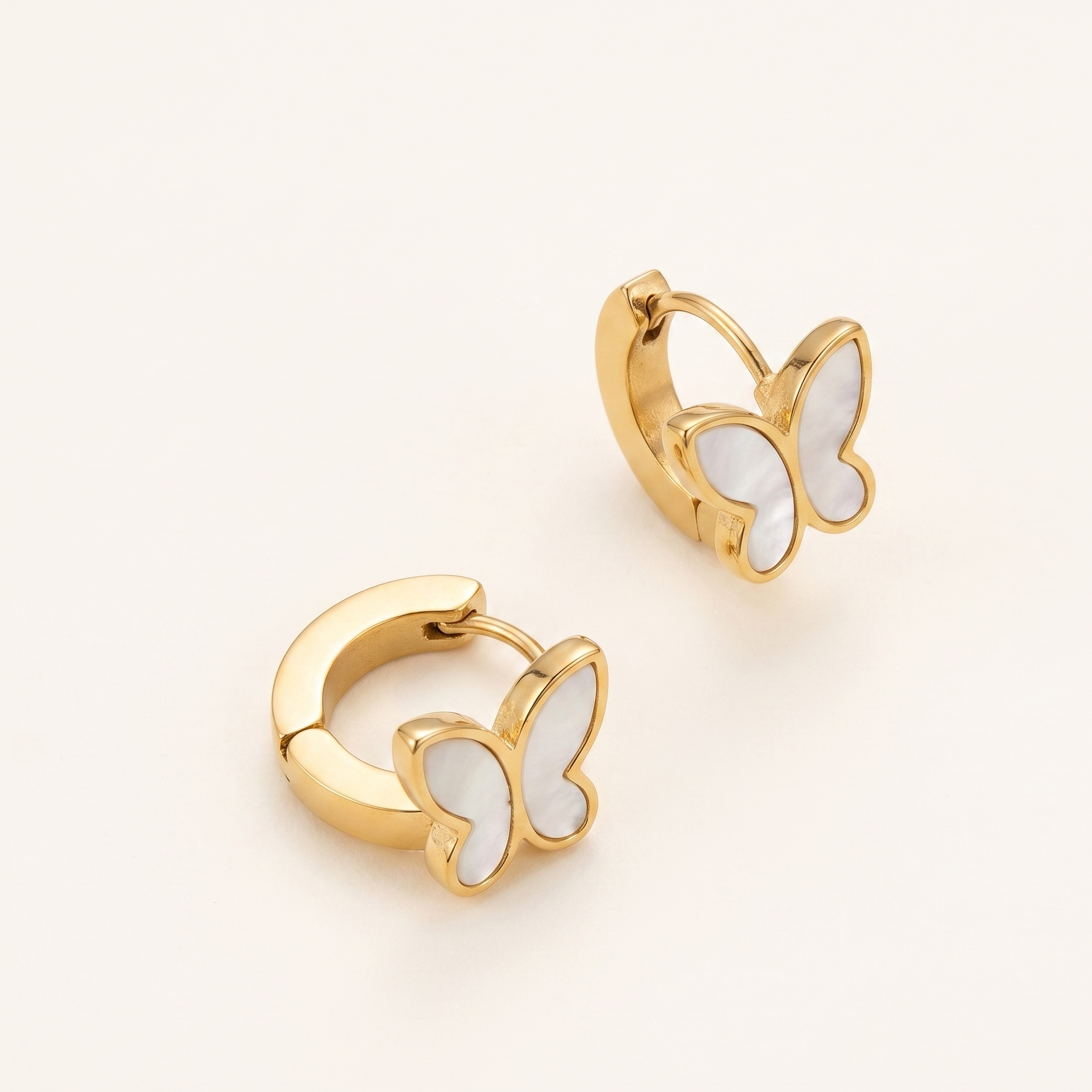 Gold butterfly earrings with white enamel on a light beige background