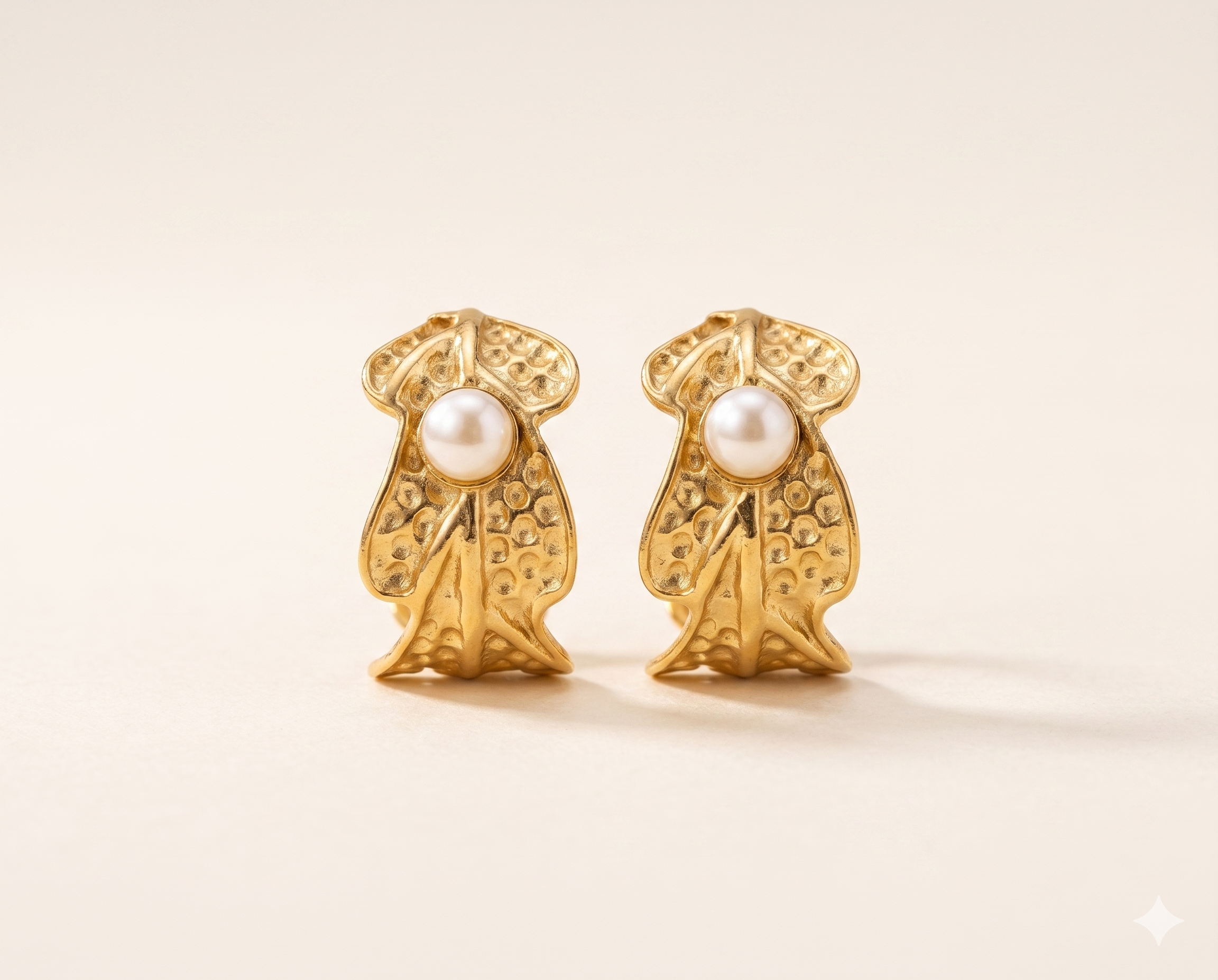 Gold earrings with pearl centers on a beige background