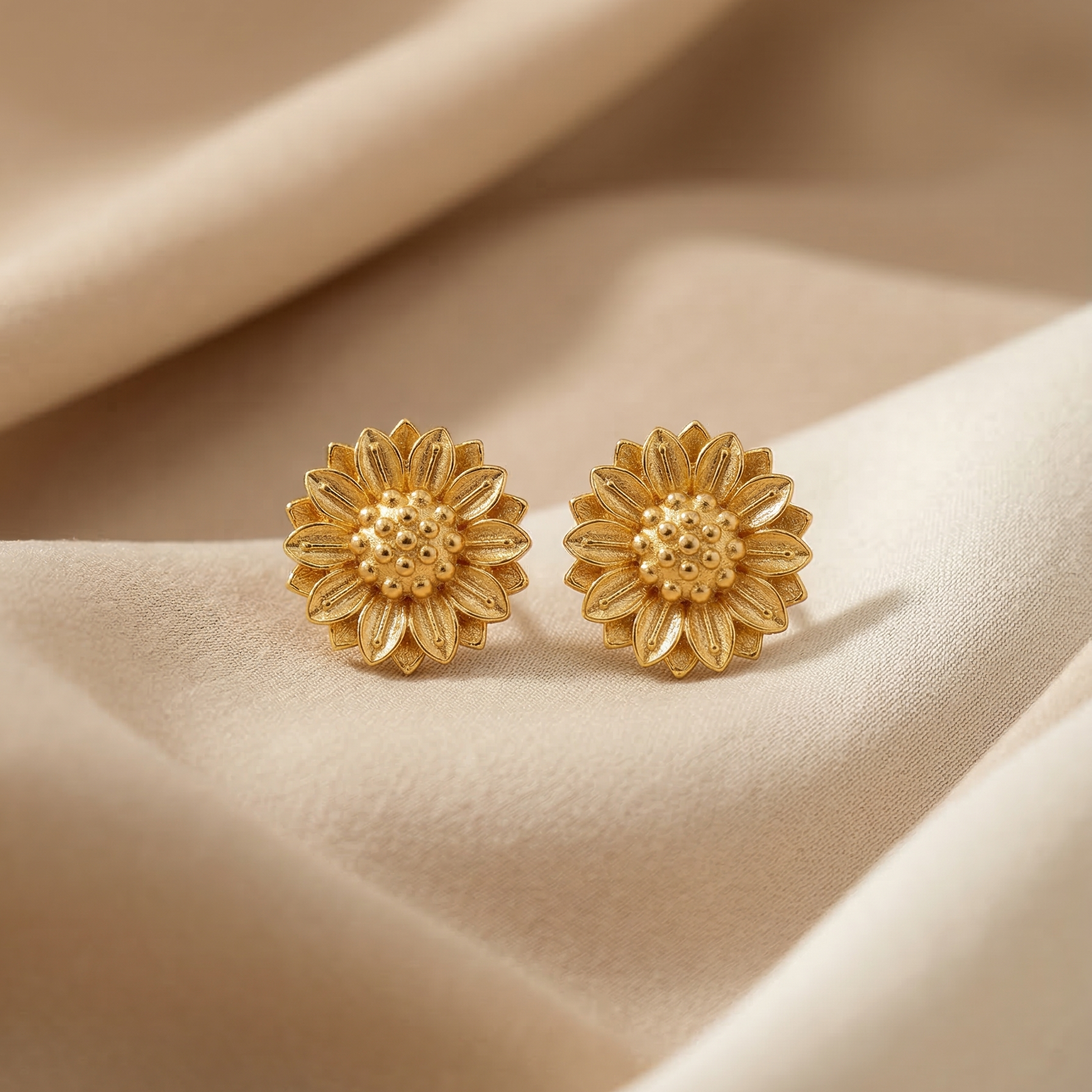 Gold flower-shaped earrings on a beige fabric background