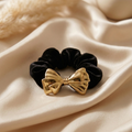 Black scrunchie with a gold bow on a beige fabric background