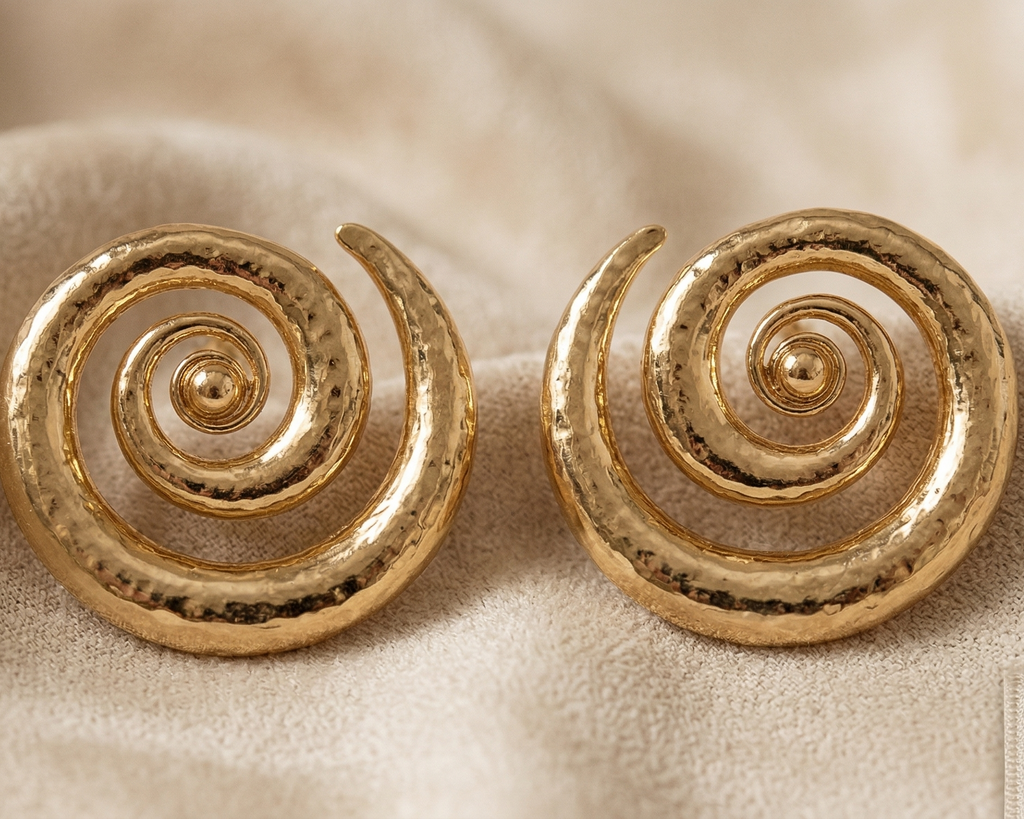 Pair of gold spiral earrings on a beige fabric background
