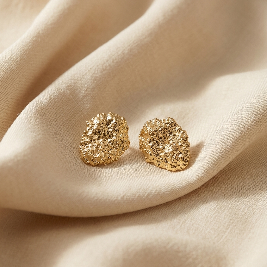 Gold textured earrings on a beige fabric surface