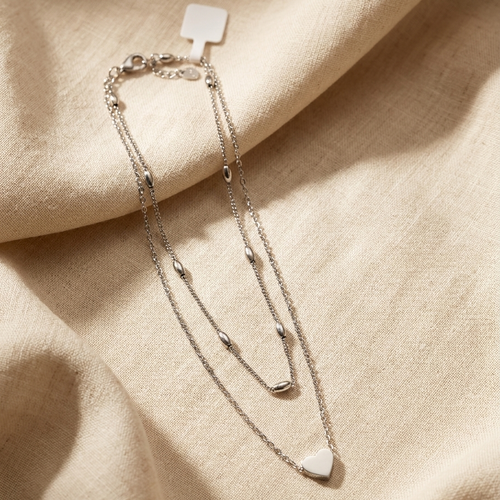 Silver bracelet with heart-shaped charm on a beige fabric background