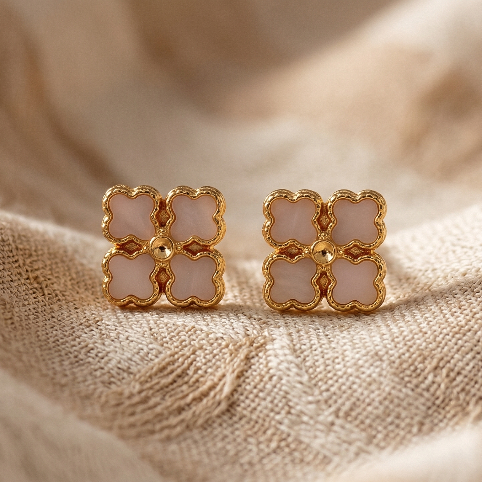 Pair of gold and white earrings on a beige fabric background