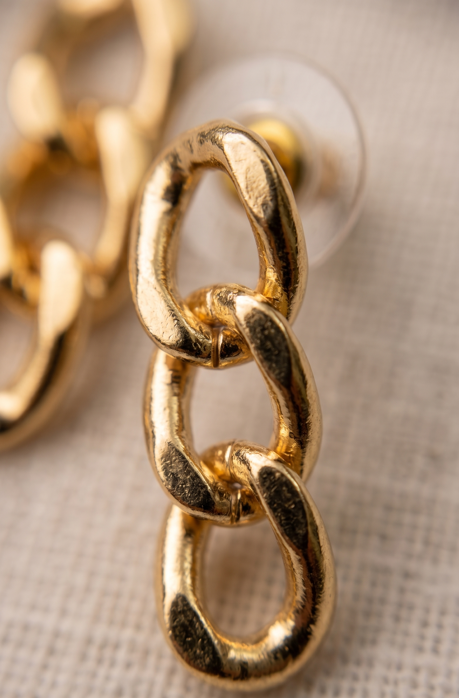 Gold chain earring on a textured beige background