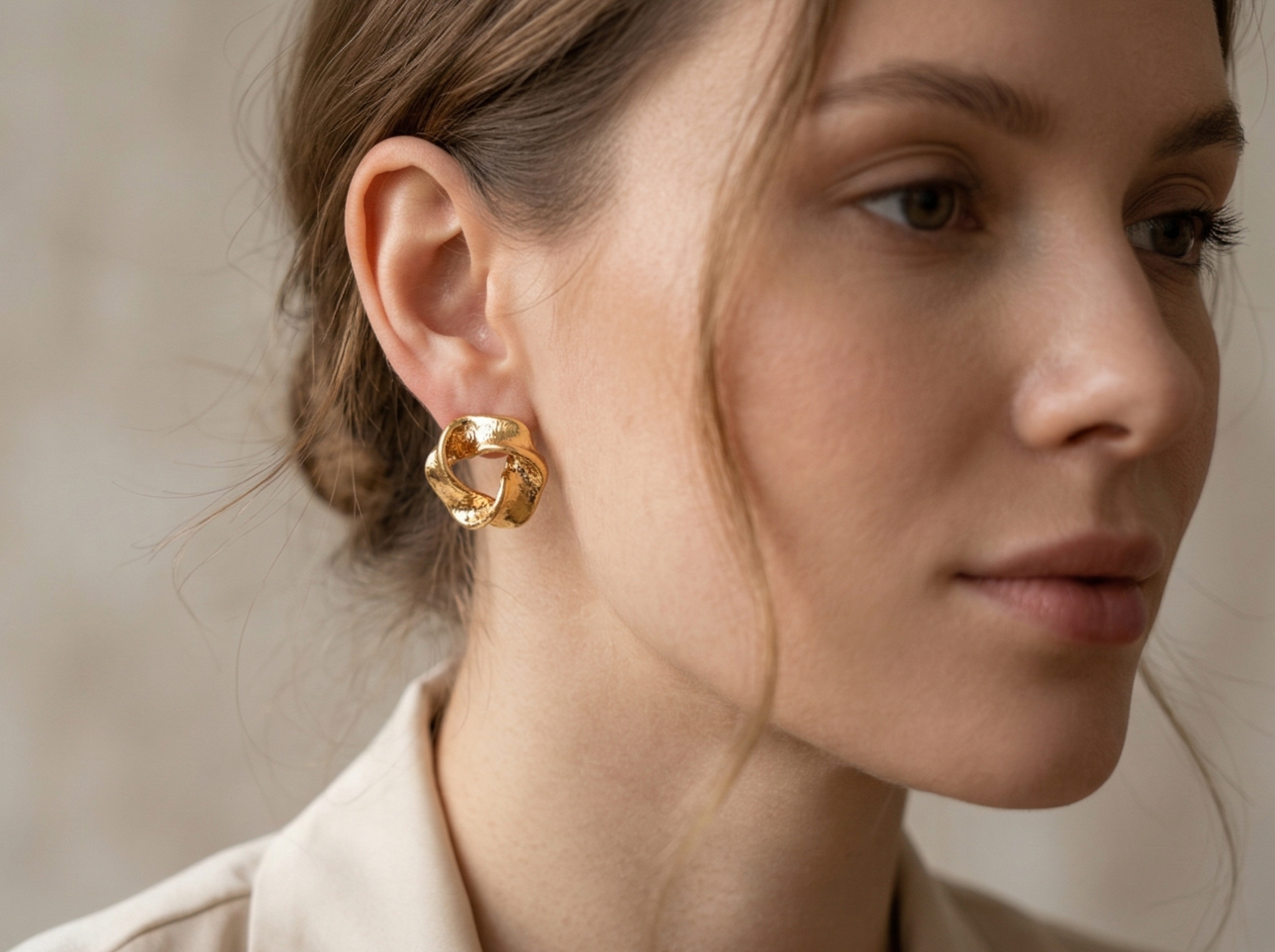 Close-up of a woman wearing gold earrings with a neutral background