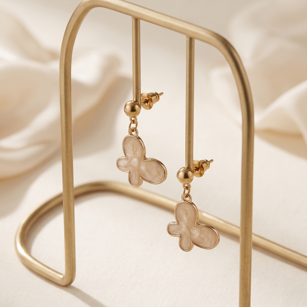 Butterfly-shaped earrings on a gold stand with a soft beige background