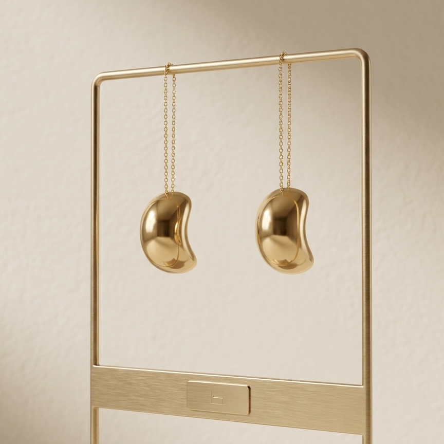 Gold earrings hanging on a gold stand against a beige background