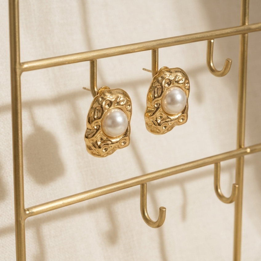 Gold earring holder with pearl earrings on a beige background