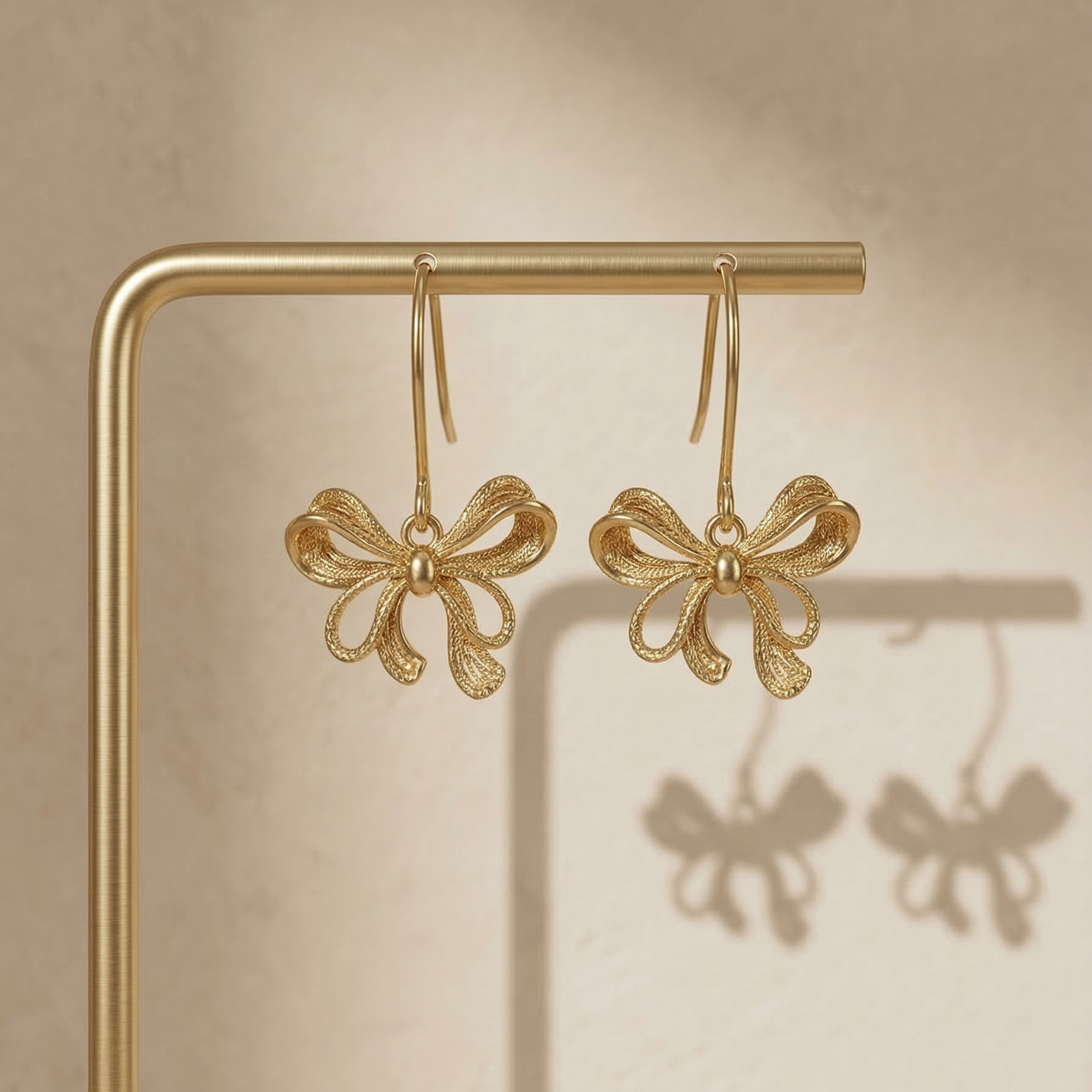 Gold bow-shaped earrings on a gold stand with a beige background