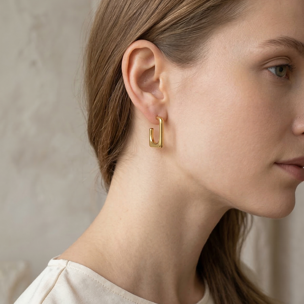 Close-up of a person wearing gold hoop earrings against a neutral background