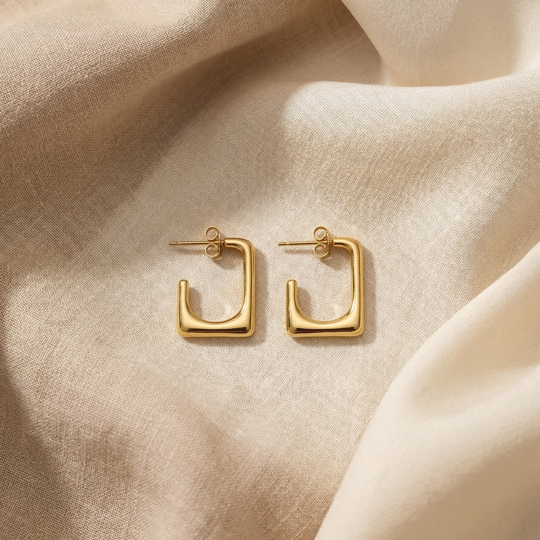Gold hoop earrings on a beige fabric background
