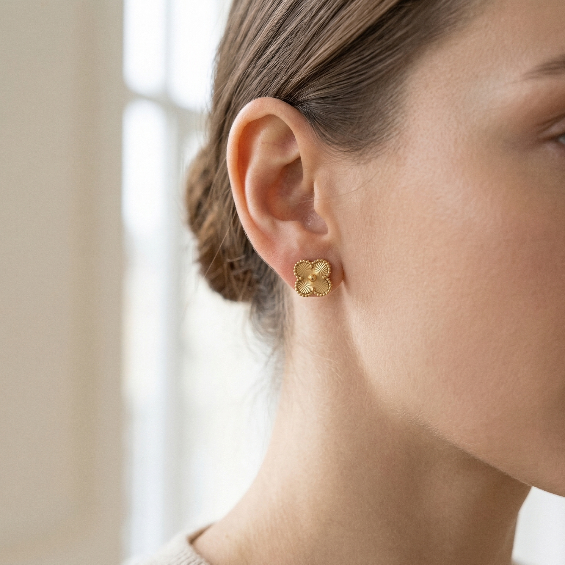 Close-up of a person wearing gold earrings with a neutral background