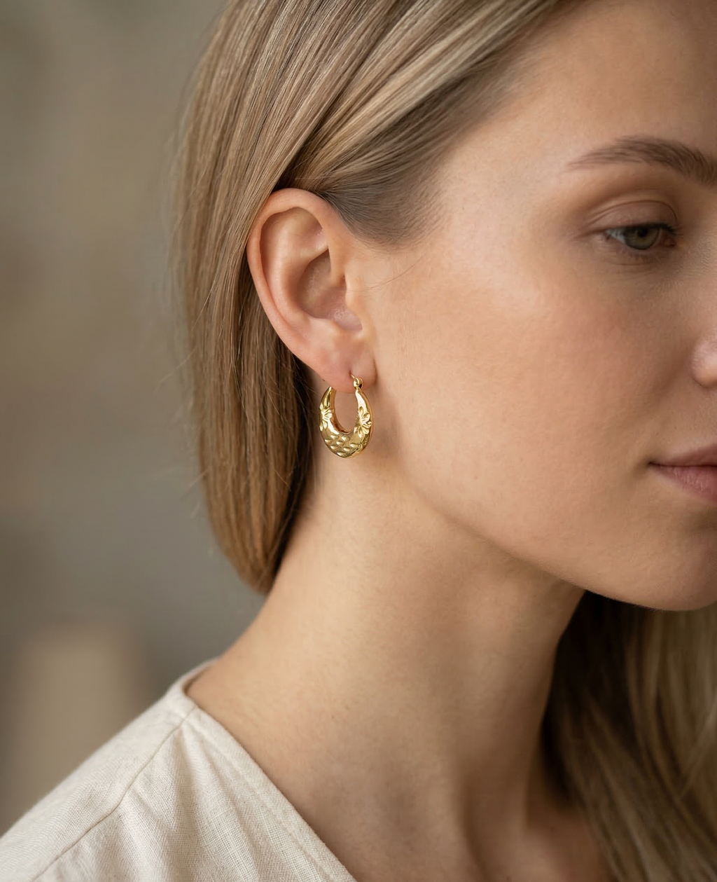 Close-up of a person wearing gold hoop earrings with a blurred background