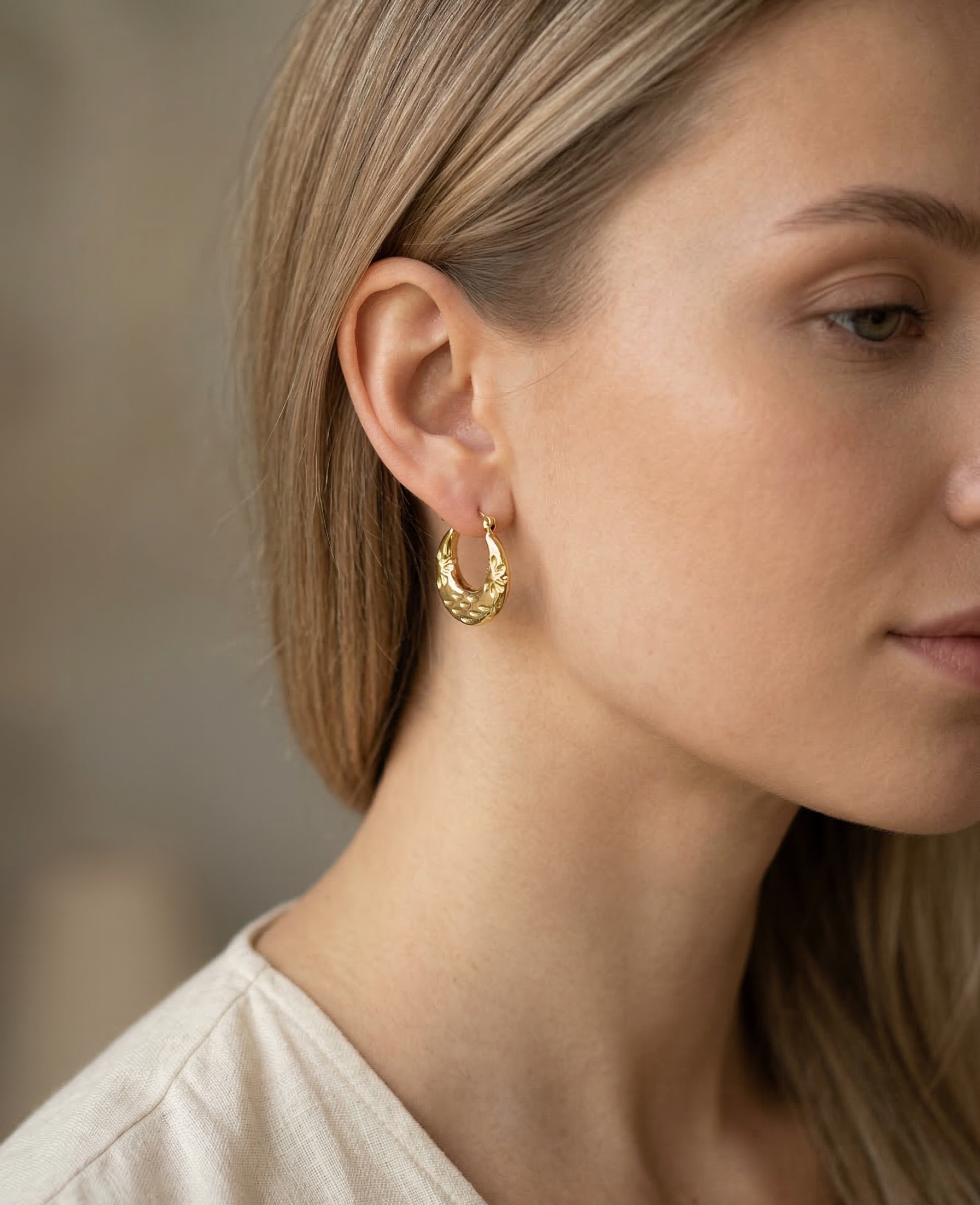 Close-up of a person wearing gold hoop earrings with a blurred background