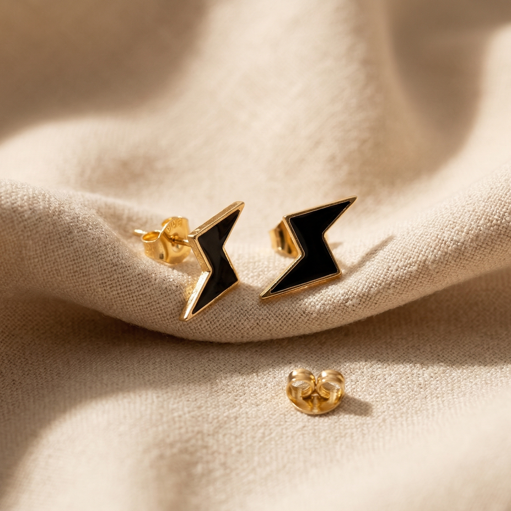 Pair of gold and black earrings on a beige fabric background