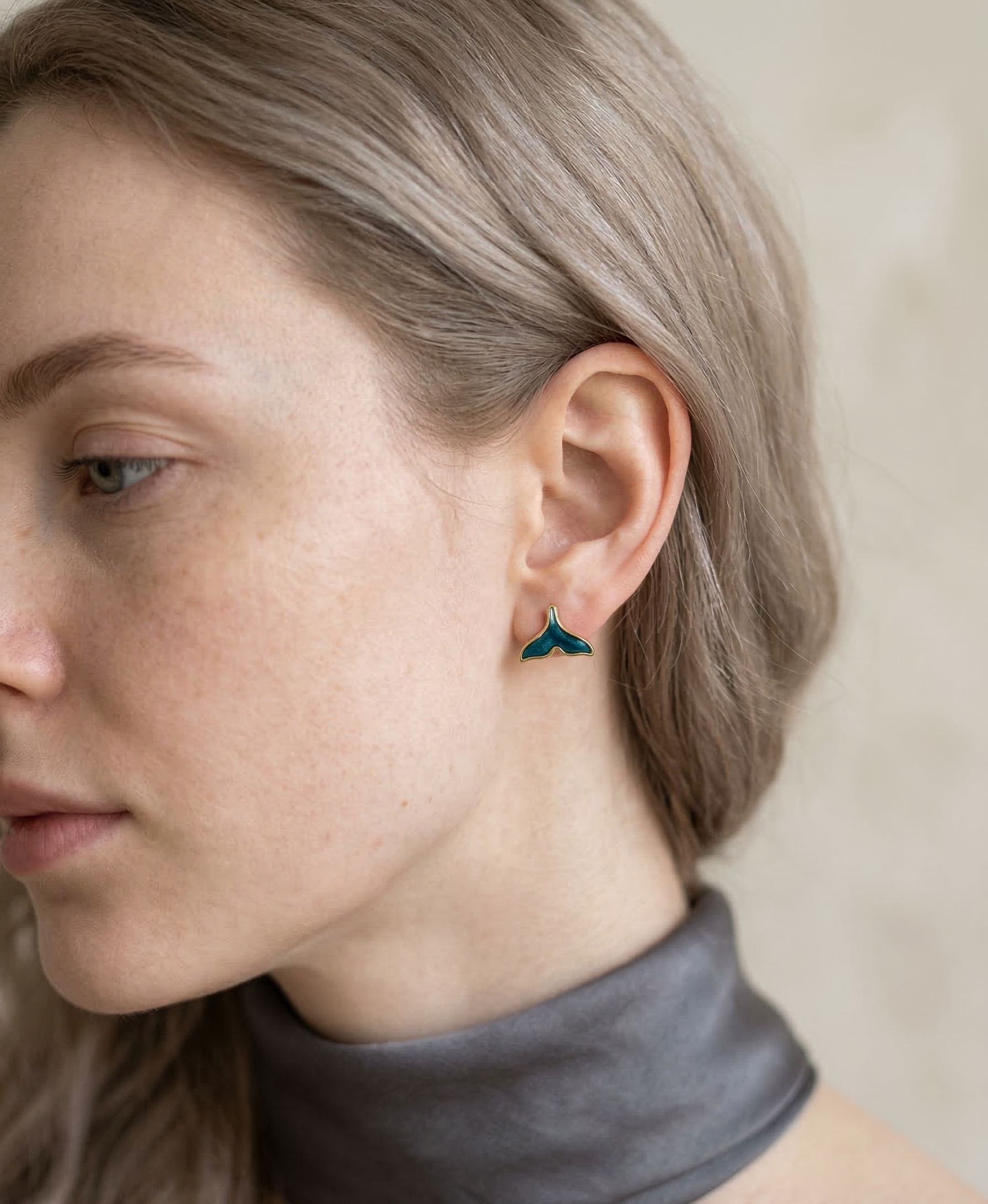 Close-up of a person wearing a teal earring with a neutral background