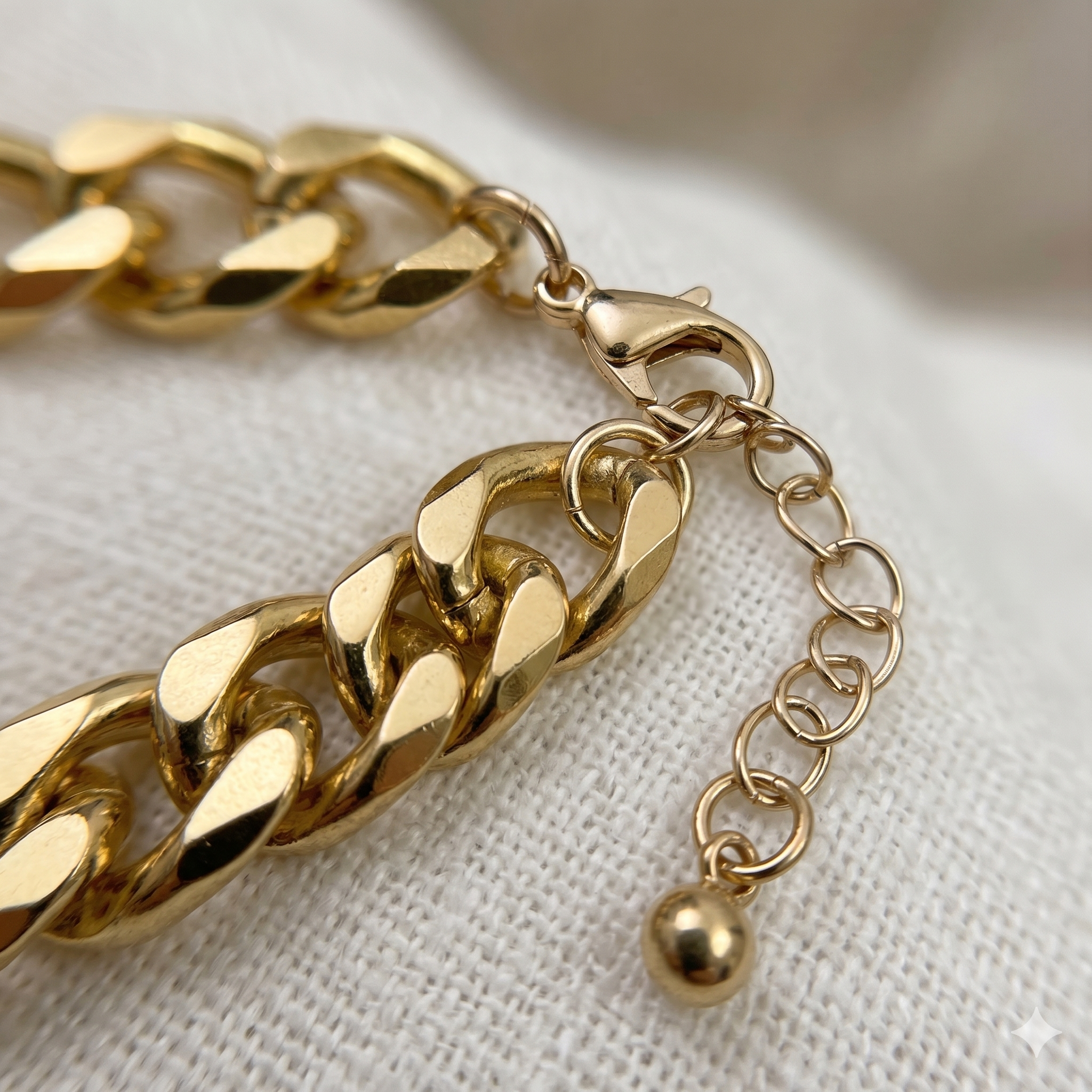 Gold chain bracelet with a small ball charm on a light fabric background