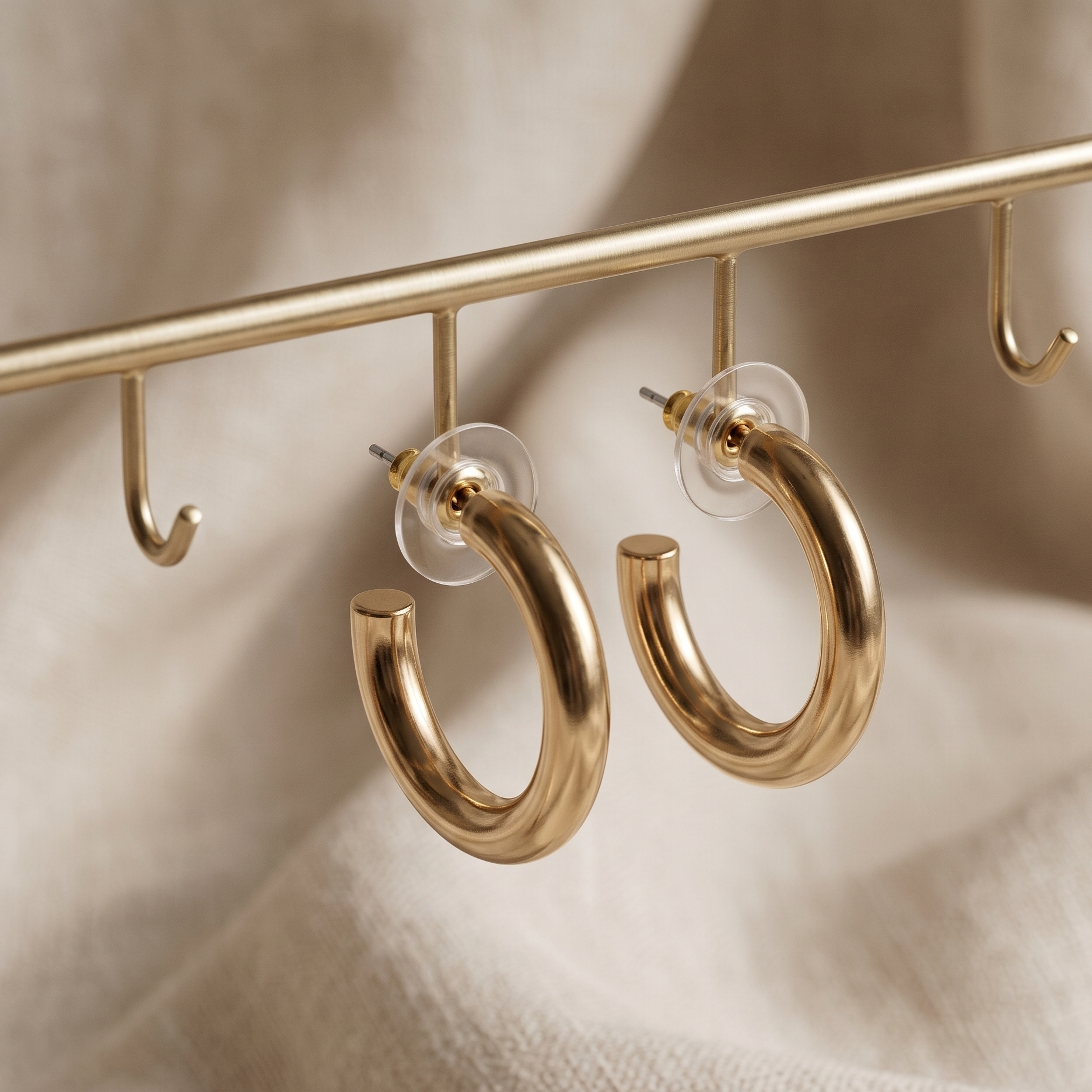 Gold hoop earrings hanging on a gold rod against a beige background