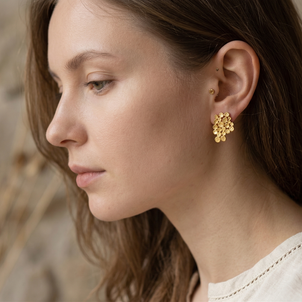 Woman wearing gold earrings with a stone wall background