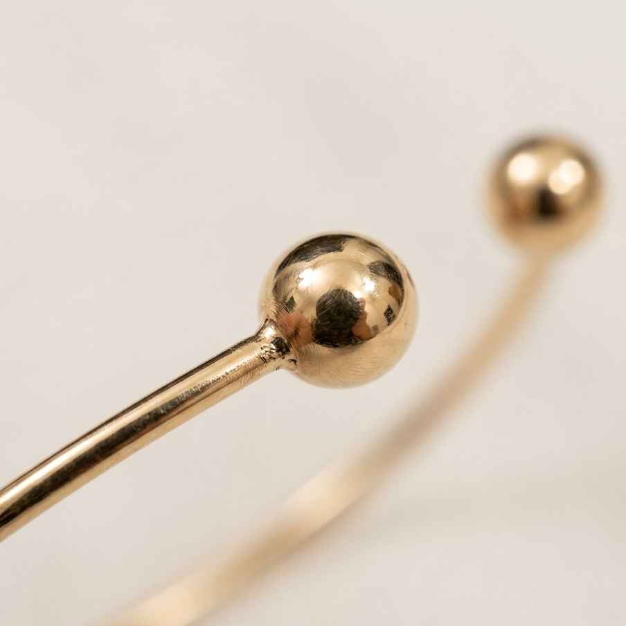 Gold bangle with spherical ends on a light beige background