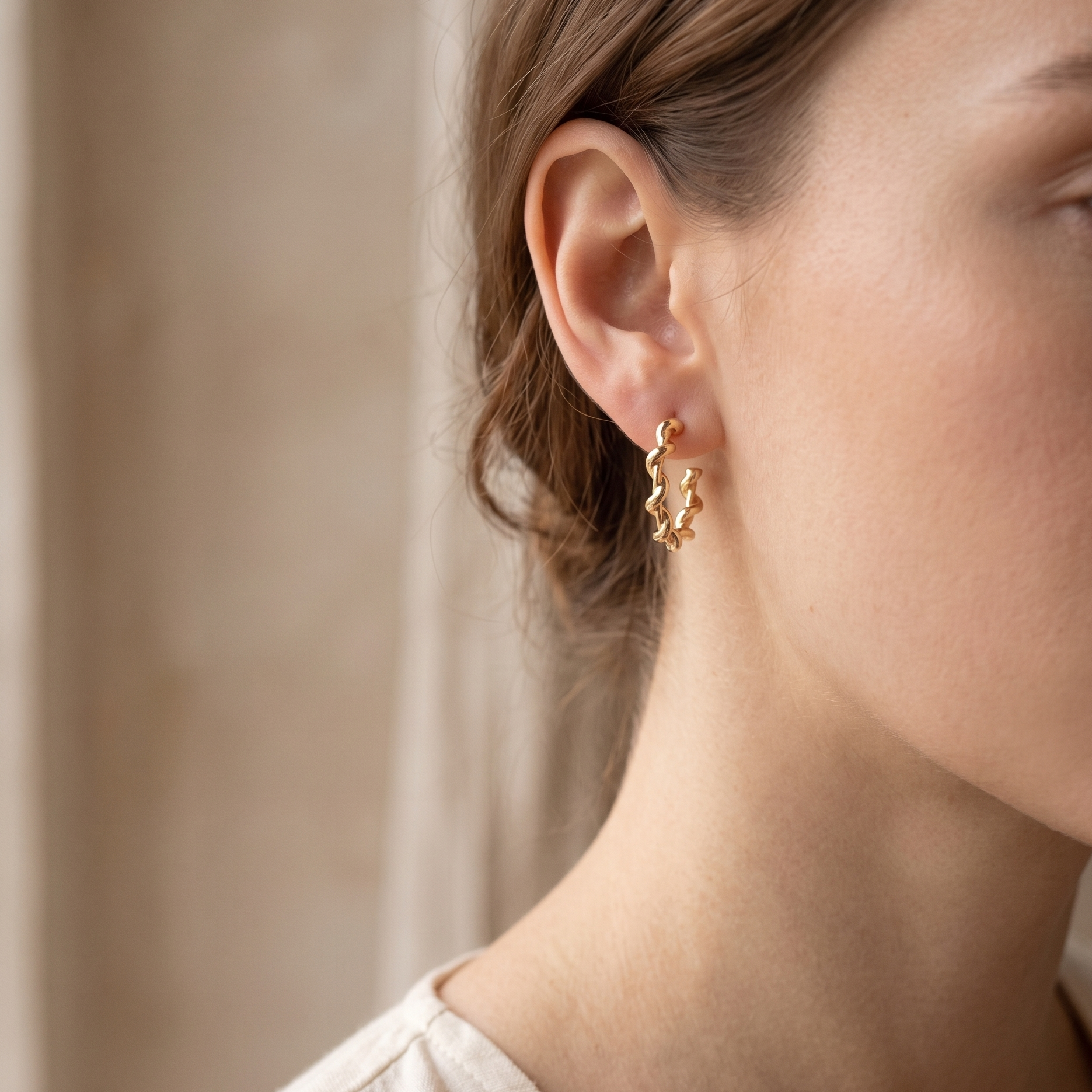 Close-up of a person wearing gold earrings with a neutral background