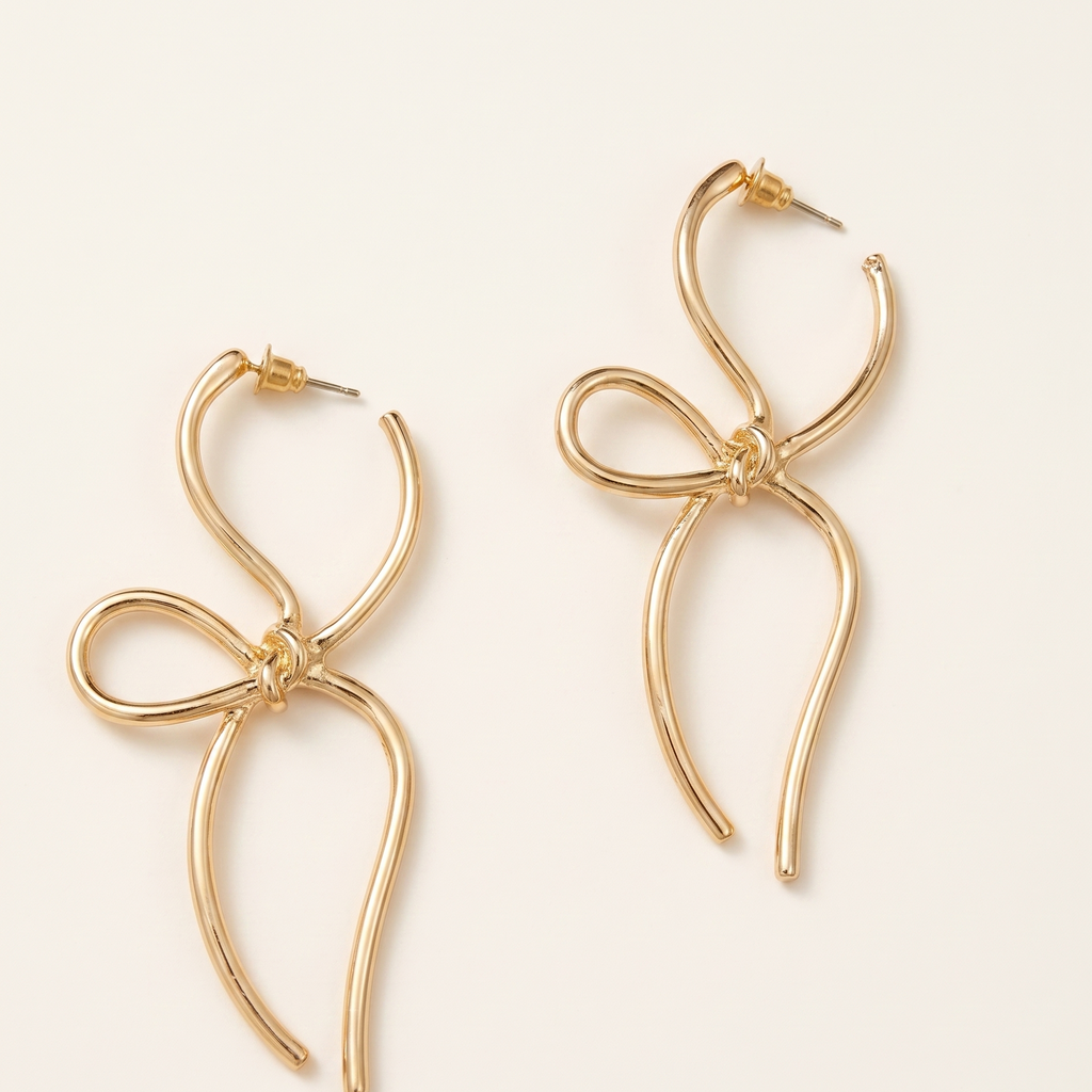 Gold bow-shaped earrings on a light beige background