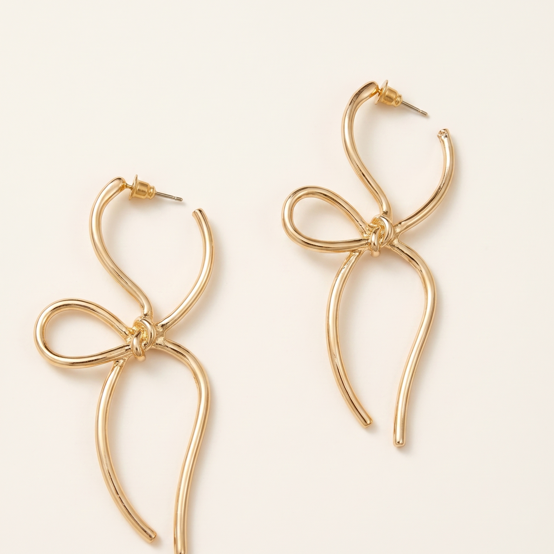 Gold bow-shaped earrings on a light beige background