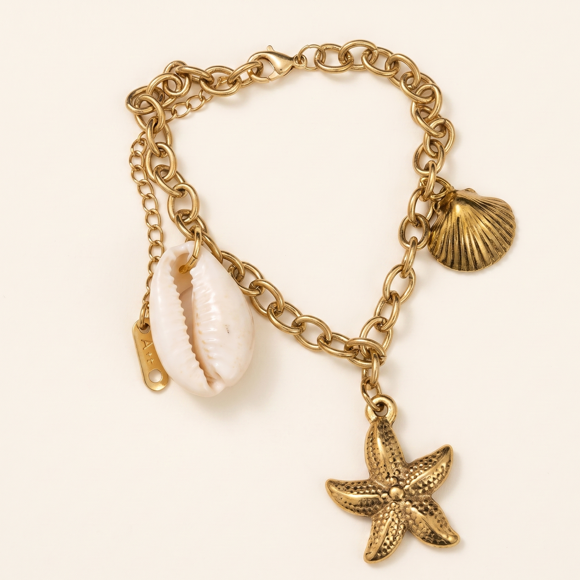 Gold chain bracelet with shell and starfish charms on a light beige background