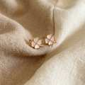 Pair of gold and pink flower-shaped earrings on beige fabric