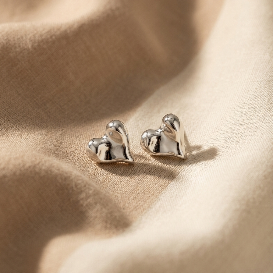 Silver heart-shaped earrings on a beige fabric background