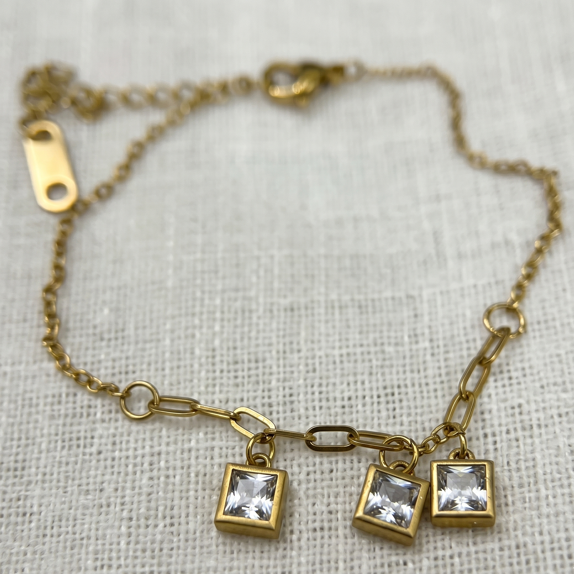 Gold bracelet with square crystal charms on a textured fabric background