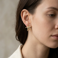 Close-up of a woman wearing gold star-shaped earrings against a neutral background