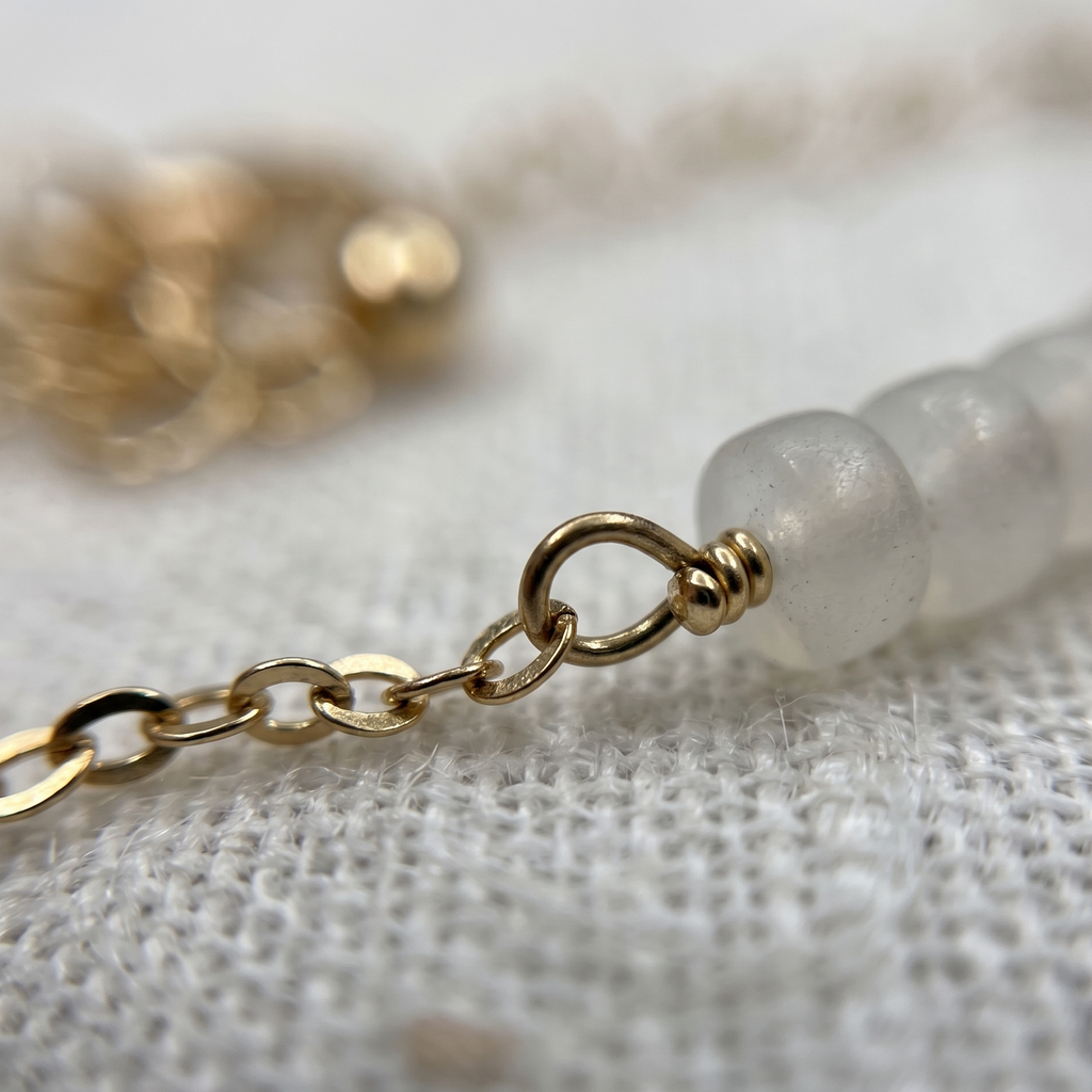 Close-up of a gold chain and white beaded bracelet on a textured surface
