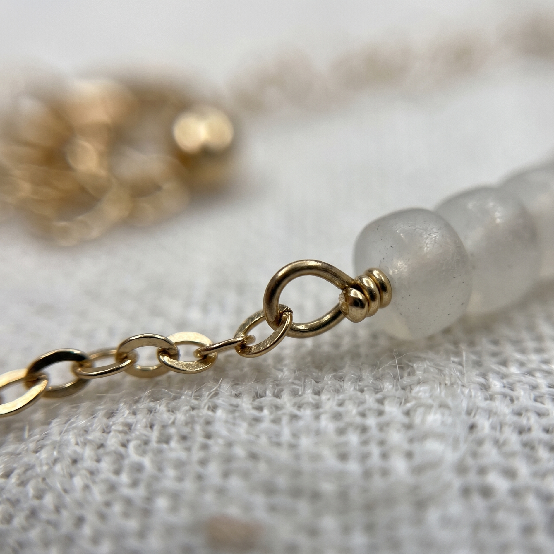 Close-up of a gold chain and white beaded bracelet on a textured surface