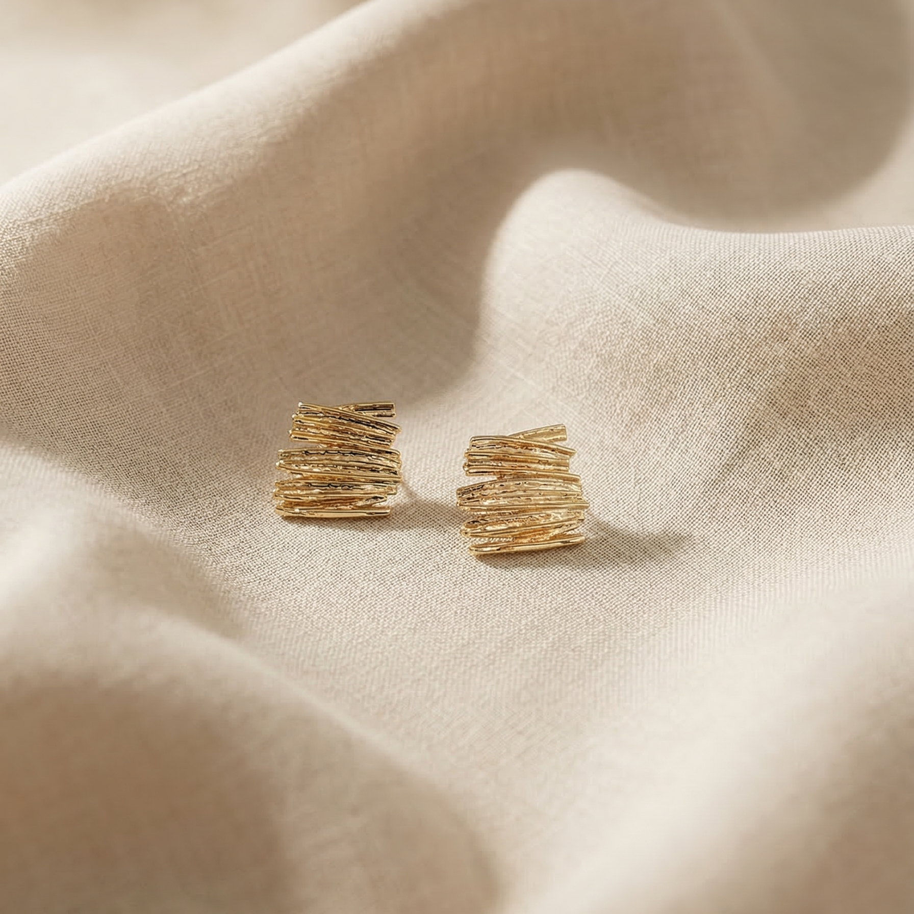 Gold earrings on a beige fabric surface