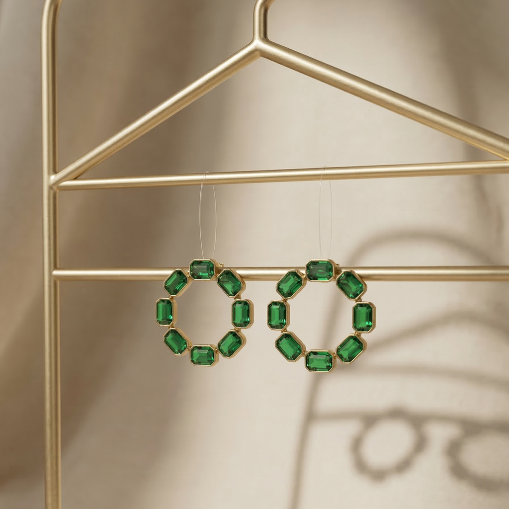 Green gemstone earrings hanging on a gold hanger against a neutral background