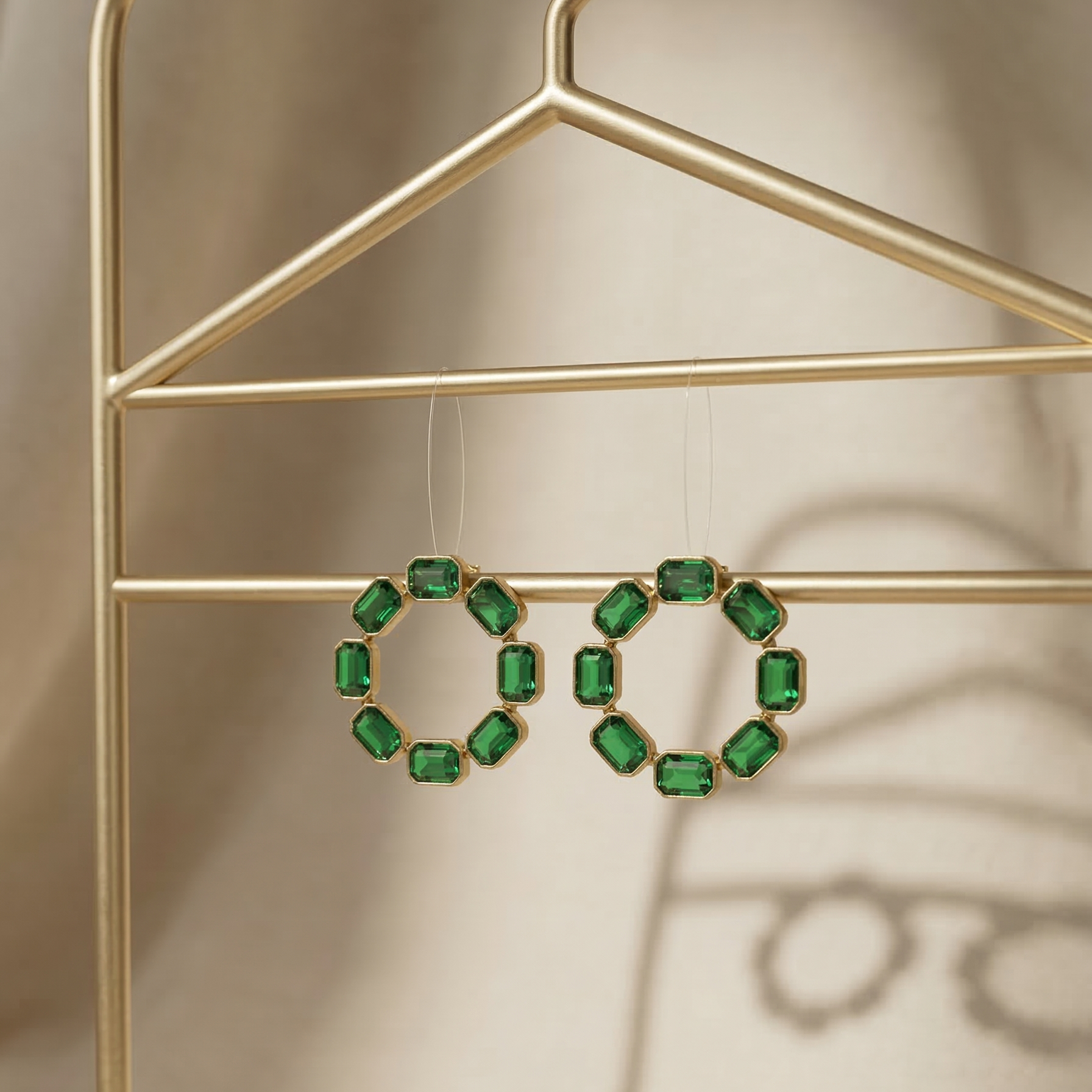 Green gemstone earrings hanging on a gold hanger against a neutral background