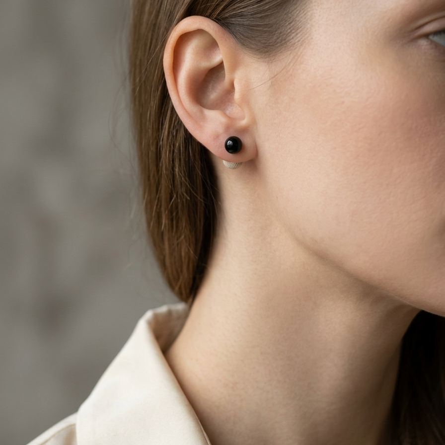 Close-up of a person wearing a black earring with a neutral background