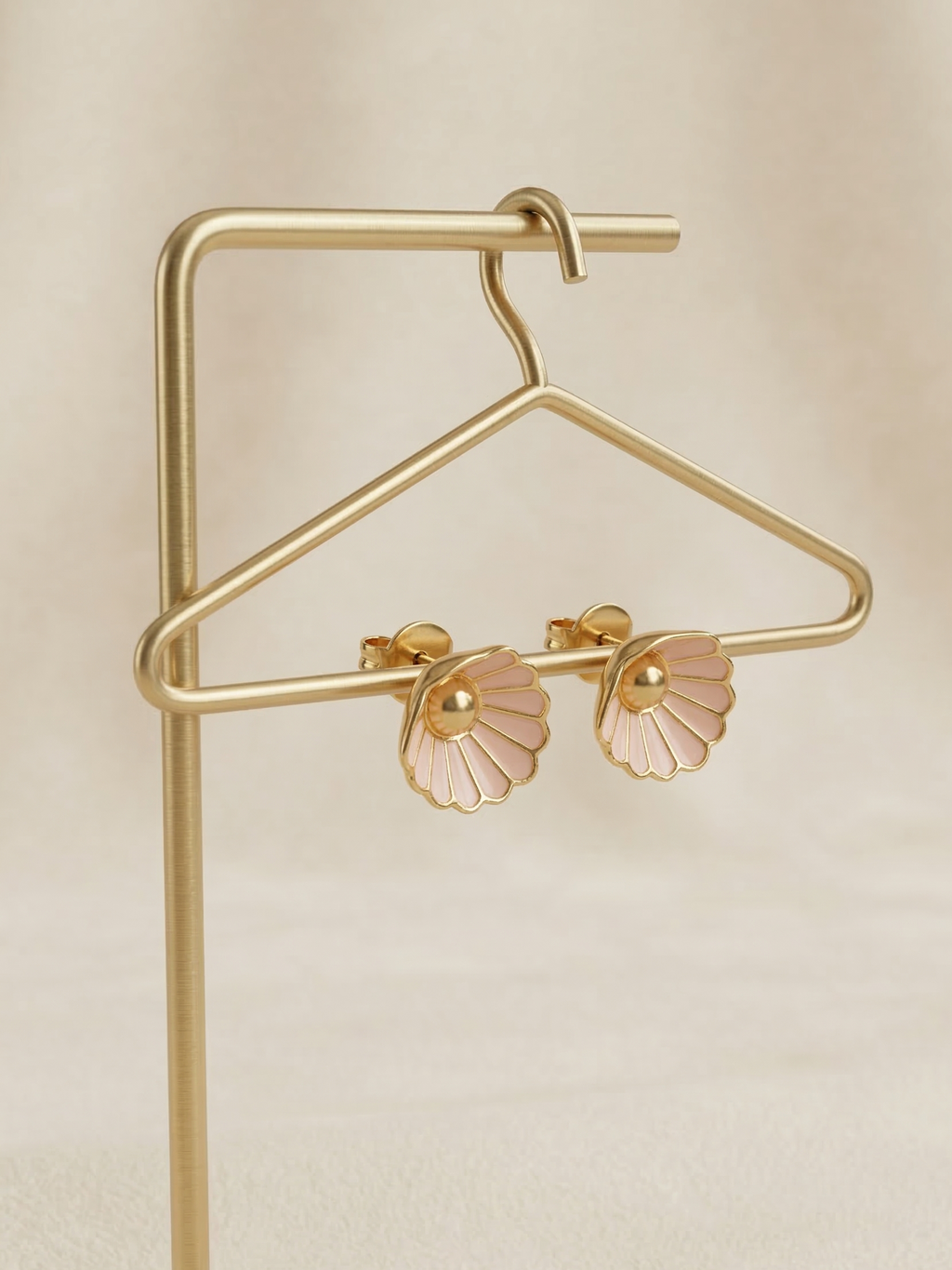 Pair of pink floral earrings on a gold hanger against a beige background