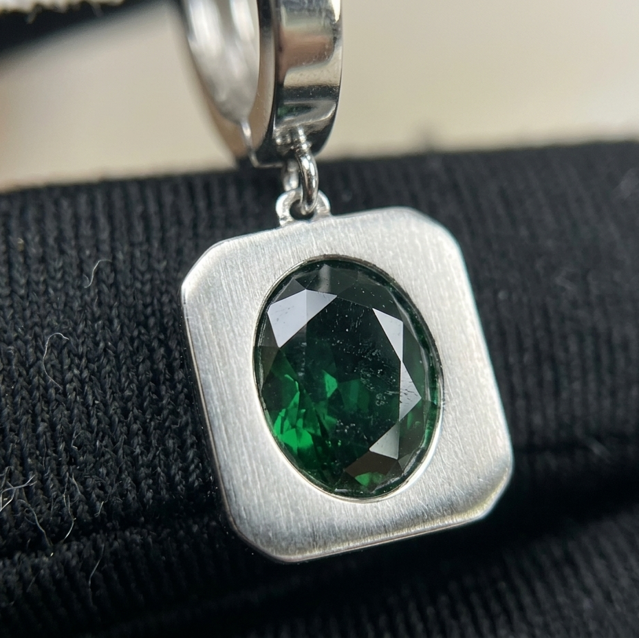 Silver pendant with a green gemstone on a black background