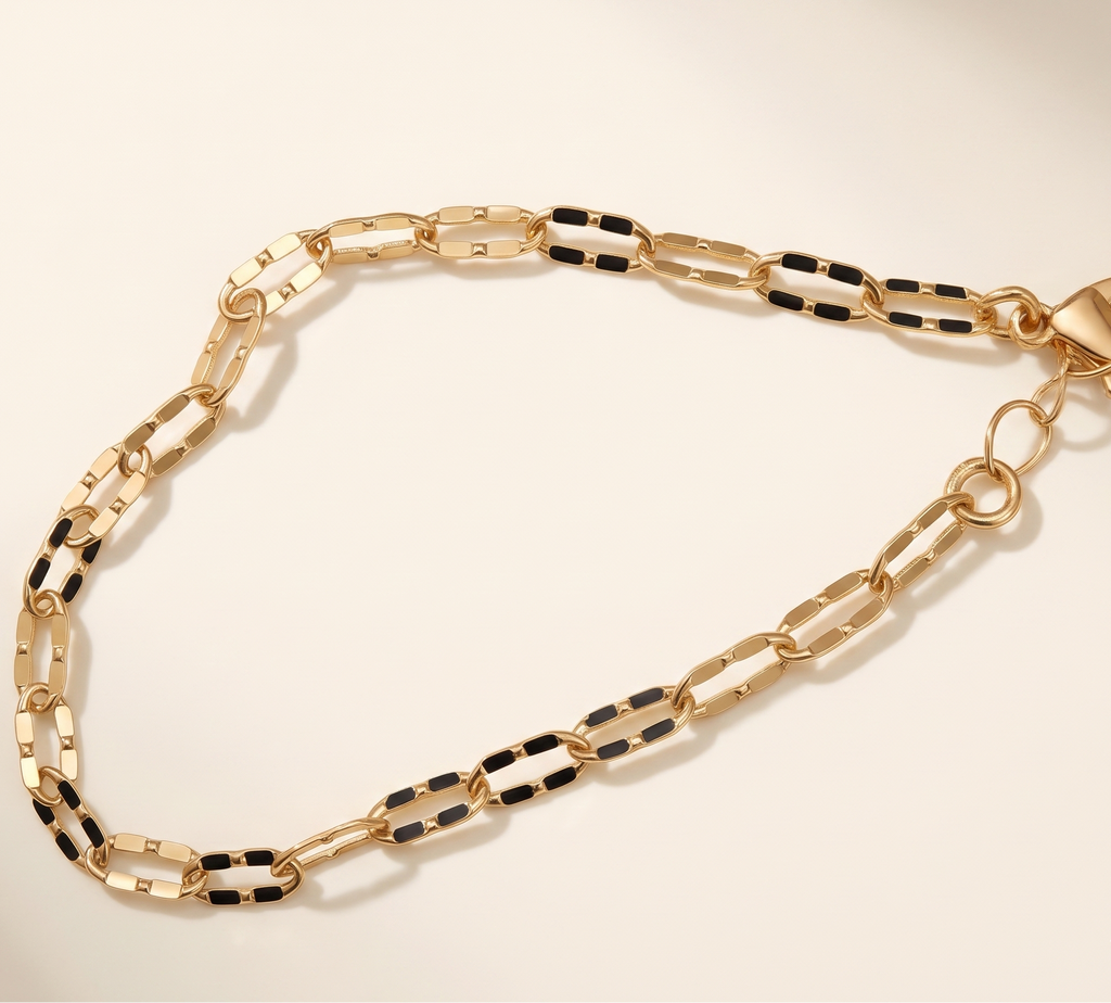 Gold chain bracelet with black accents on a beige background