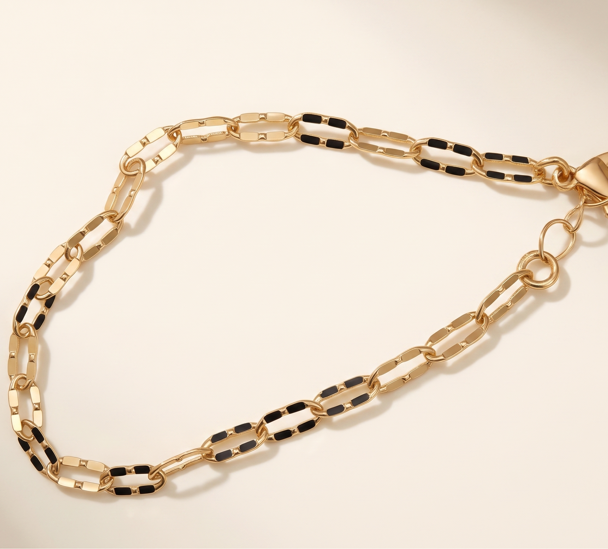 Gold chain bracelet with black accents on a beige background
