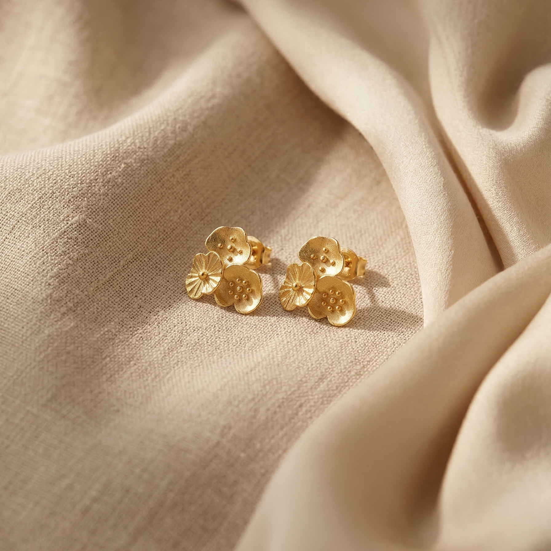 Gold floral earrings on beige fabric