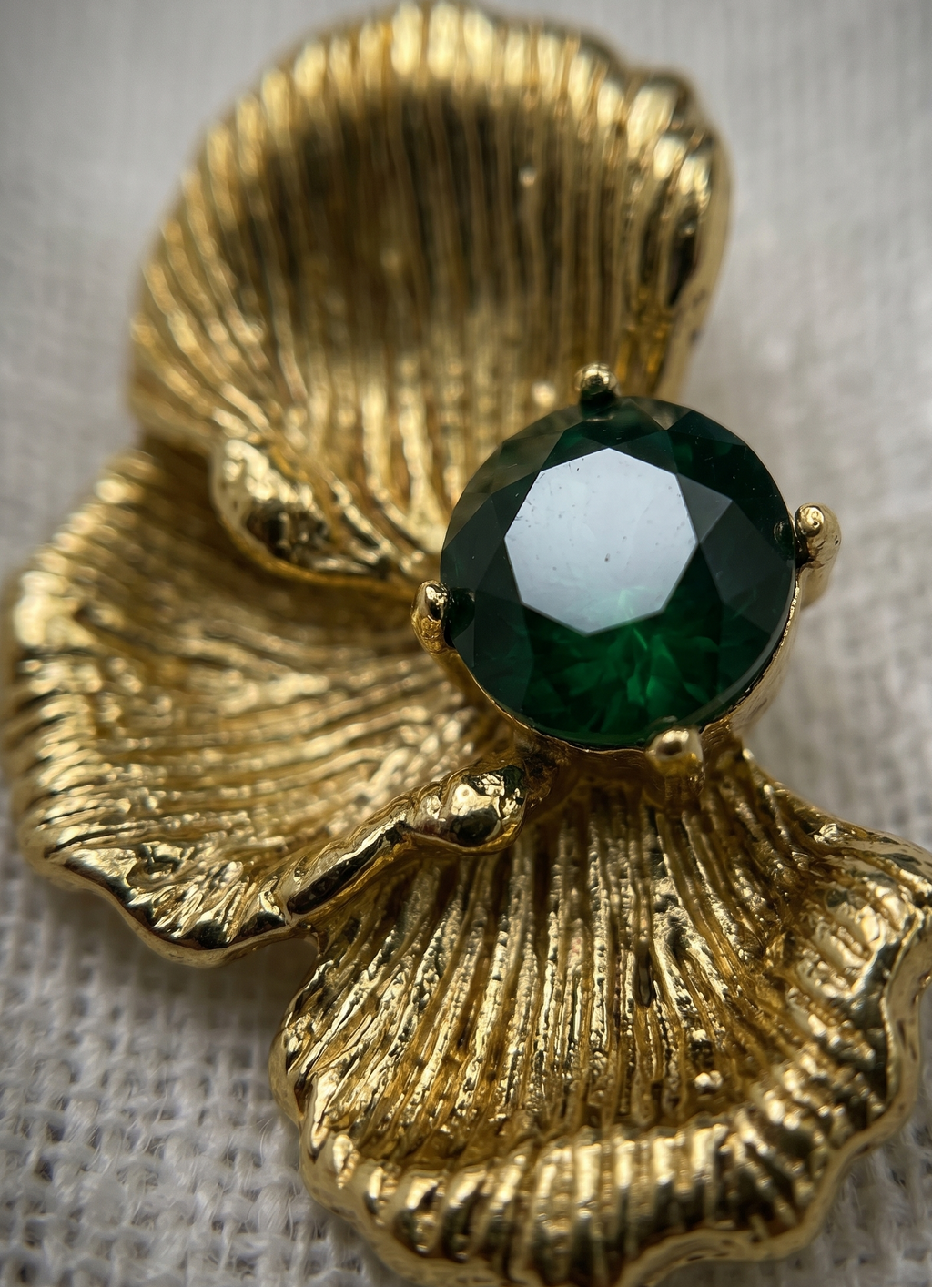 Gold shell-shaped brooch with a green gemstone on a textured fabric background