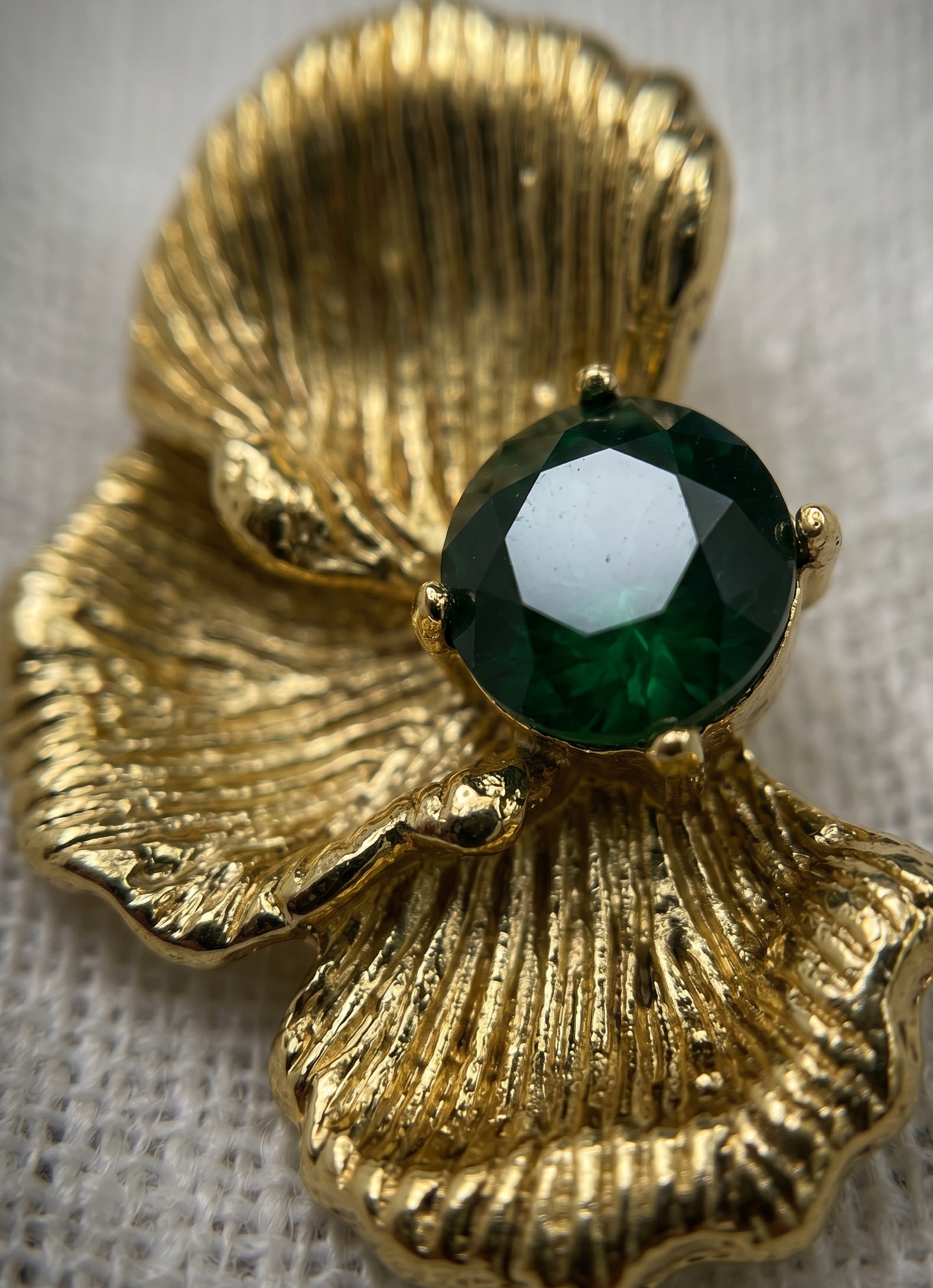 Gold shell-shaped brooch with a green gemstone on a textured fabric background