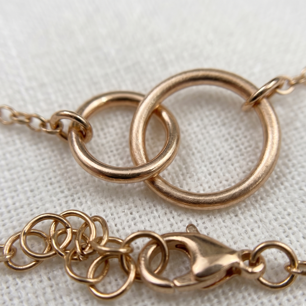 Rose gold bracelet with interlocking rings on a white fabric background