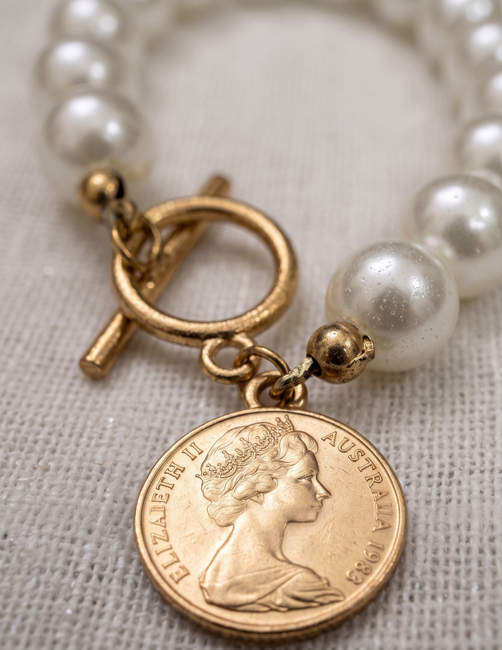 Pearl necklace with a gold coin charm featuring a portrait on a textured fabric background