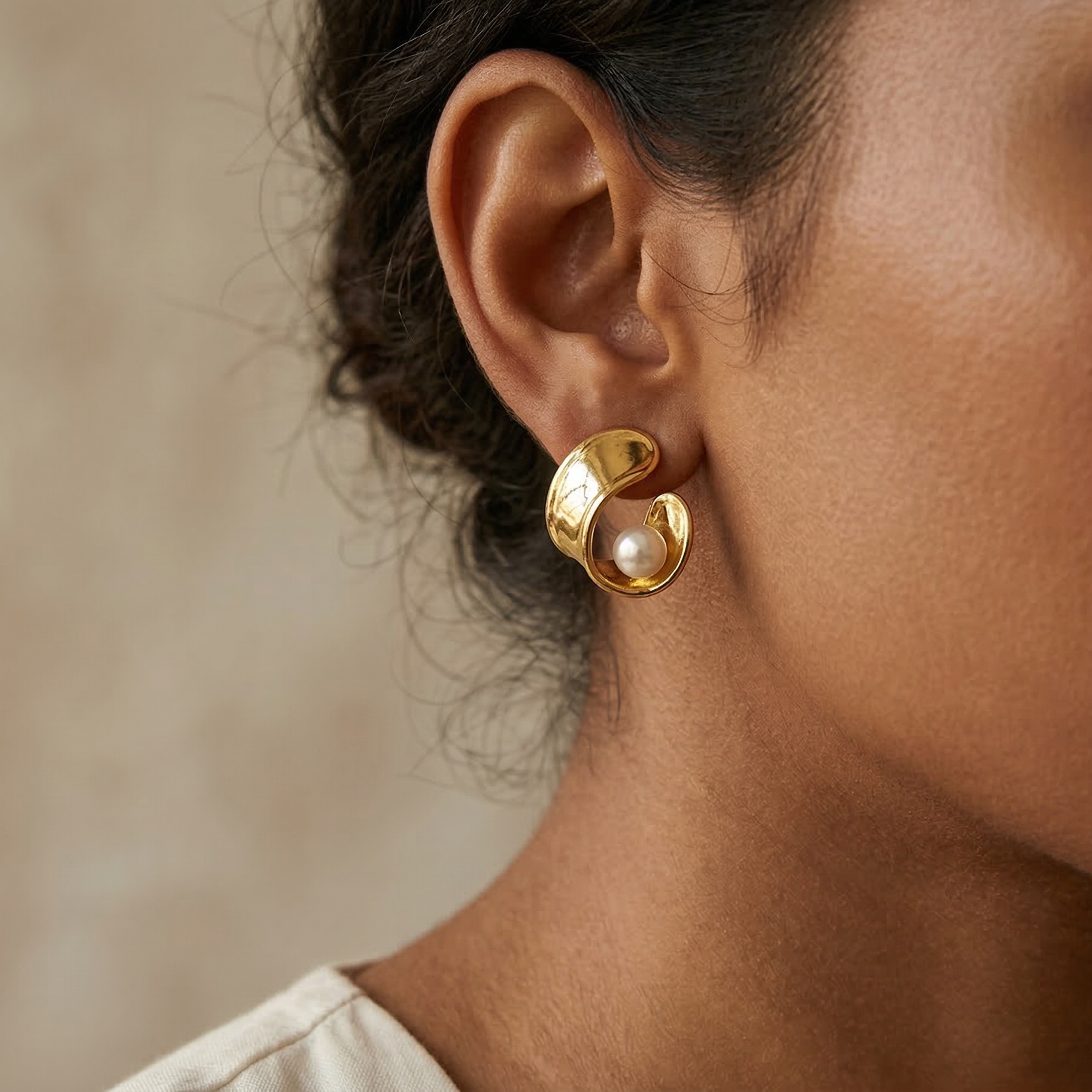 Gold earring with pearl detail worn by a person against a neutral background