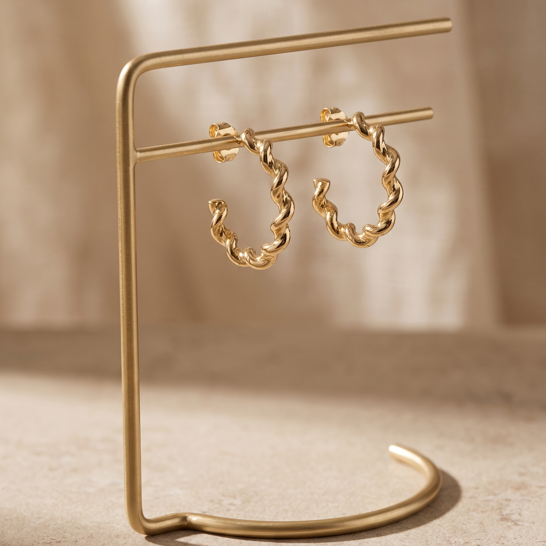 Gold chain hoop earrings on a matching gold stand against a beige background